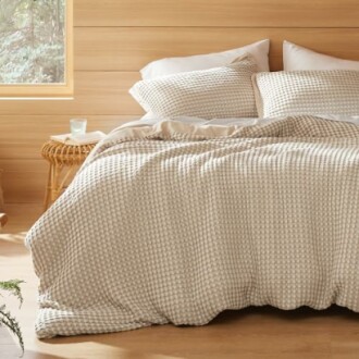 Cozy bedroom with a checkered comforter and pillows on a wooden bed.