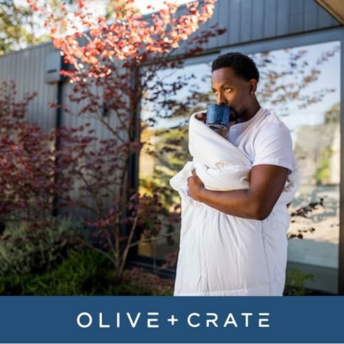 Man holding a blanket and drinking from a mug outside.