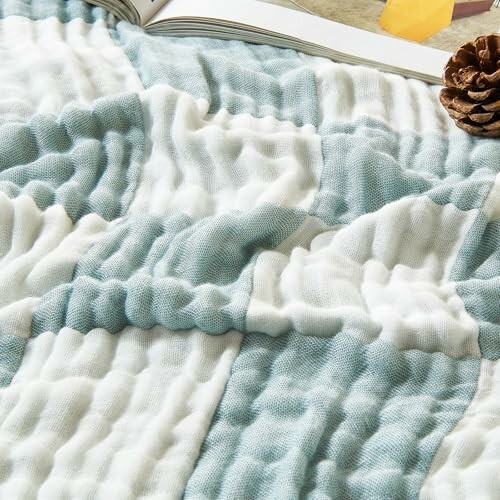 Close-up of a textured blanket with a book and pinecone nearby.