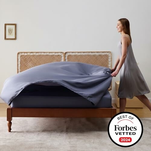 Woman making a bed with a gray duvet cover, Best of Forbes Vetted 2024 badge.