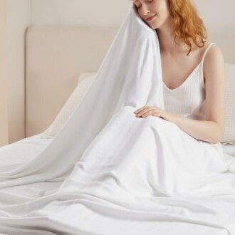 Woman in white dress sitting on a bed with a white sheet.