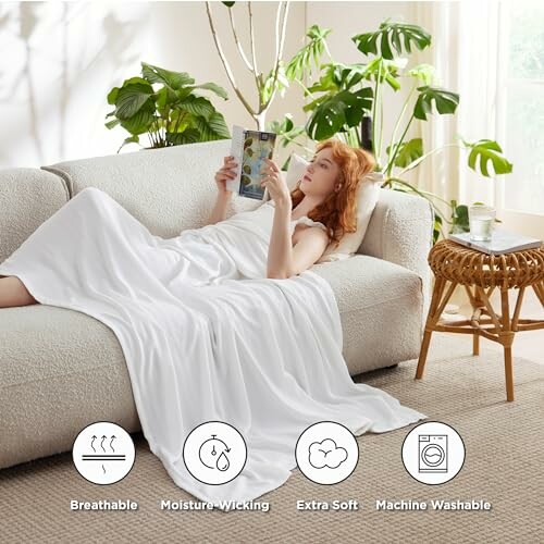 Woman reading on sofa with white blanket in bright room